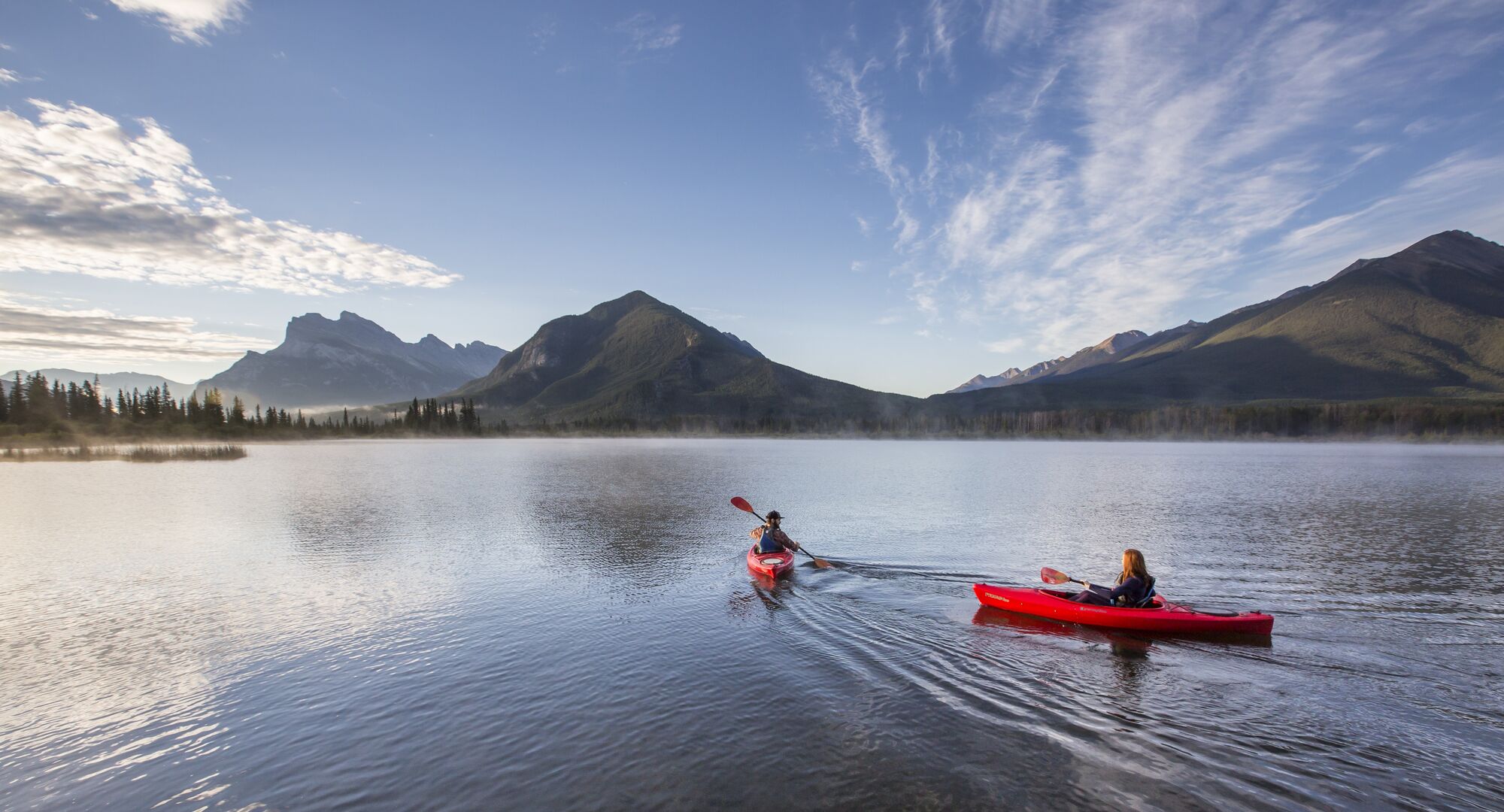 Two people in kayaks paddling on Vermilion Lakes at sunrise